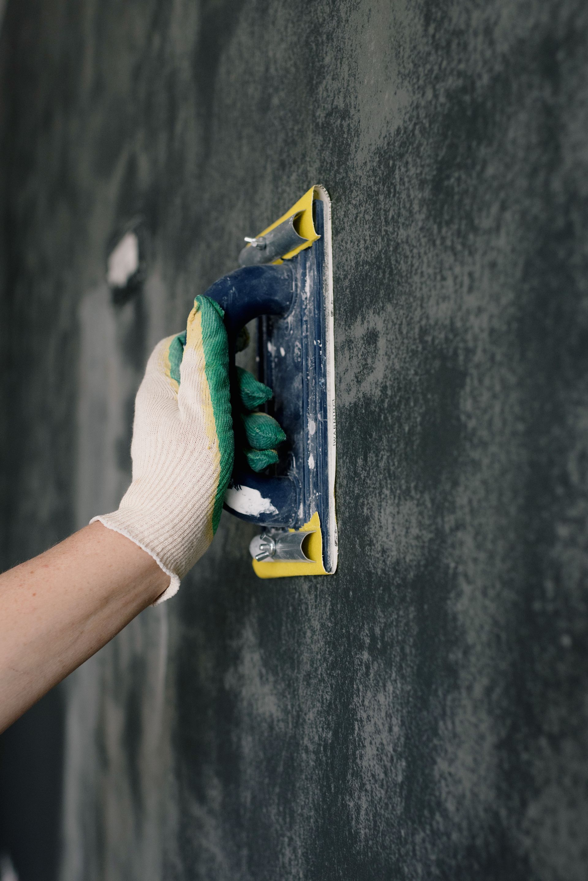 Hand sanding a wall during surface preparation for property maintenance