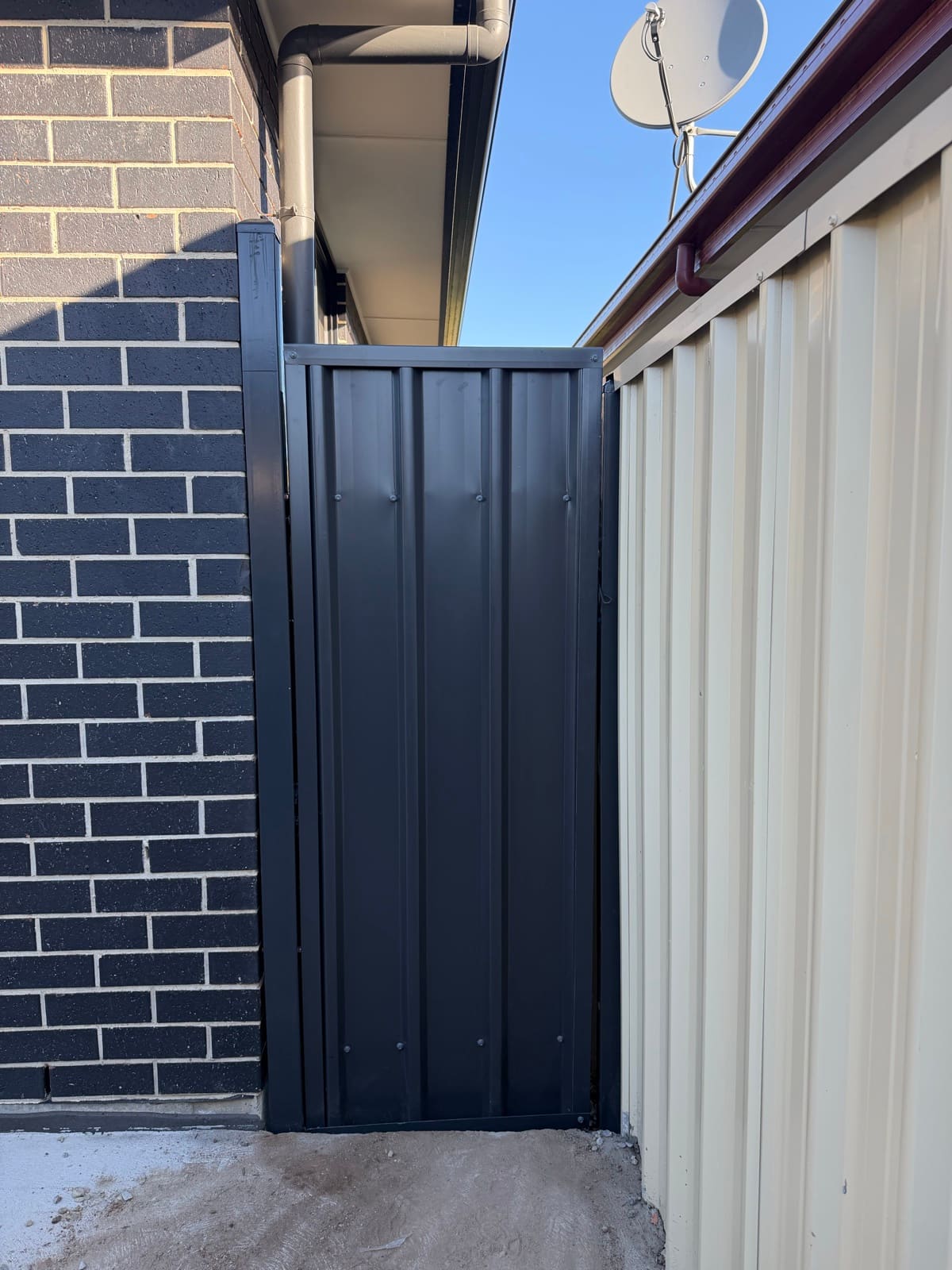 Charcoal corrugated metal side gate installed between a brick wall and cream Colorbond fence
