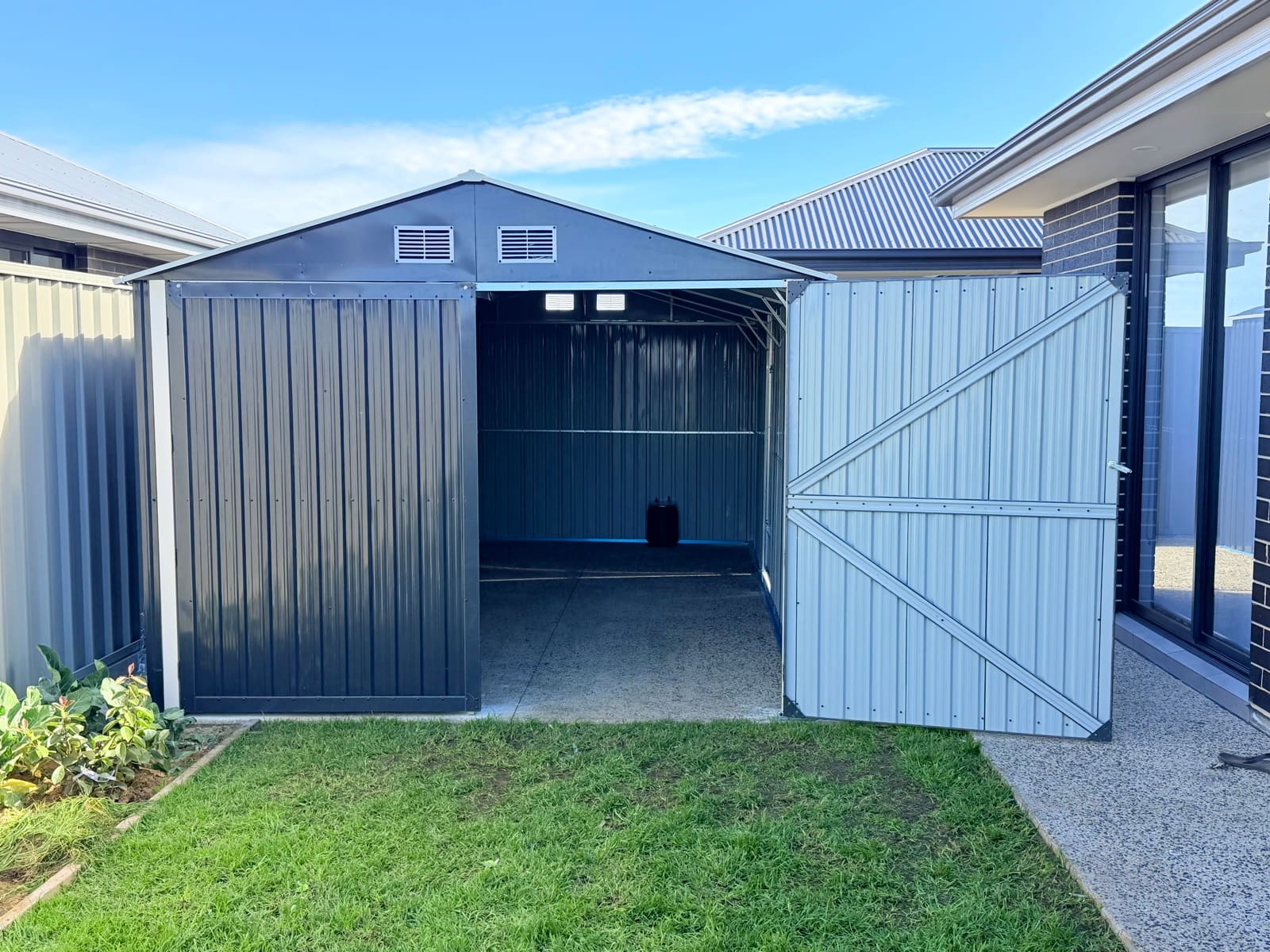 Metal garden shed with double doors open showing the concrete floor and braced door panels in Adelaide