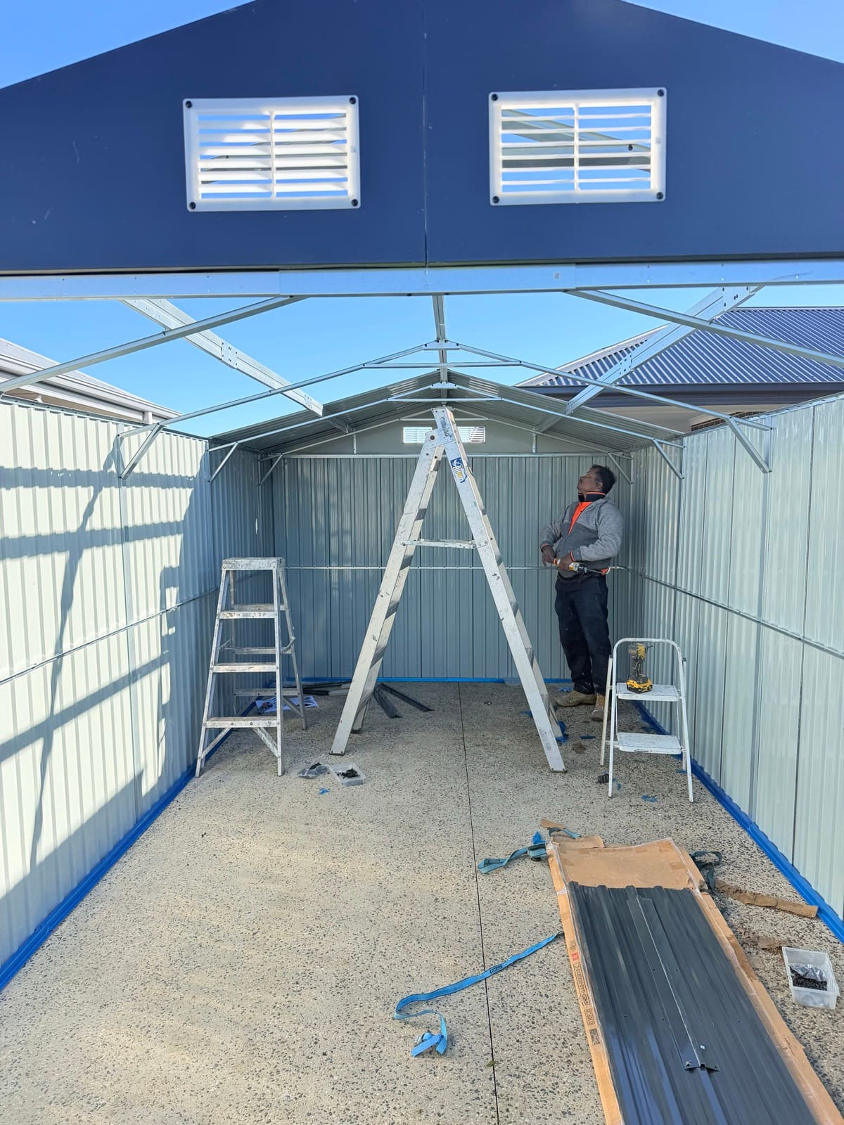 Metal garden shed walls and roof frame under assembly on a concrete slab in an Adelaide backyard