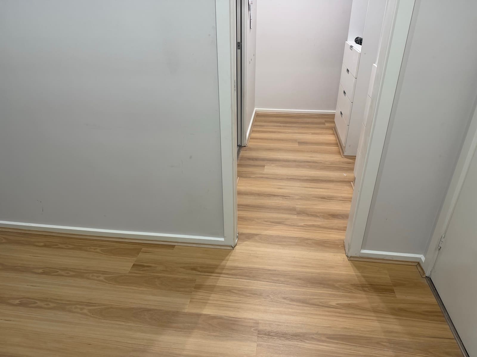 Newly installed light wood flooring continuing from a room into a hallway with white skirting