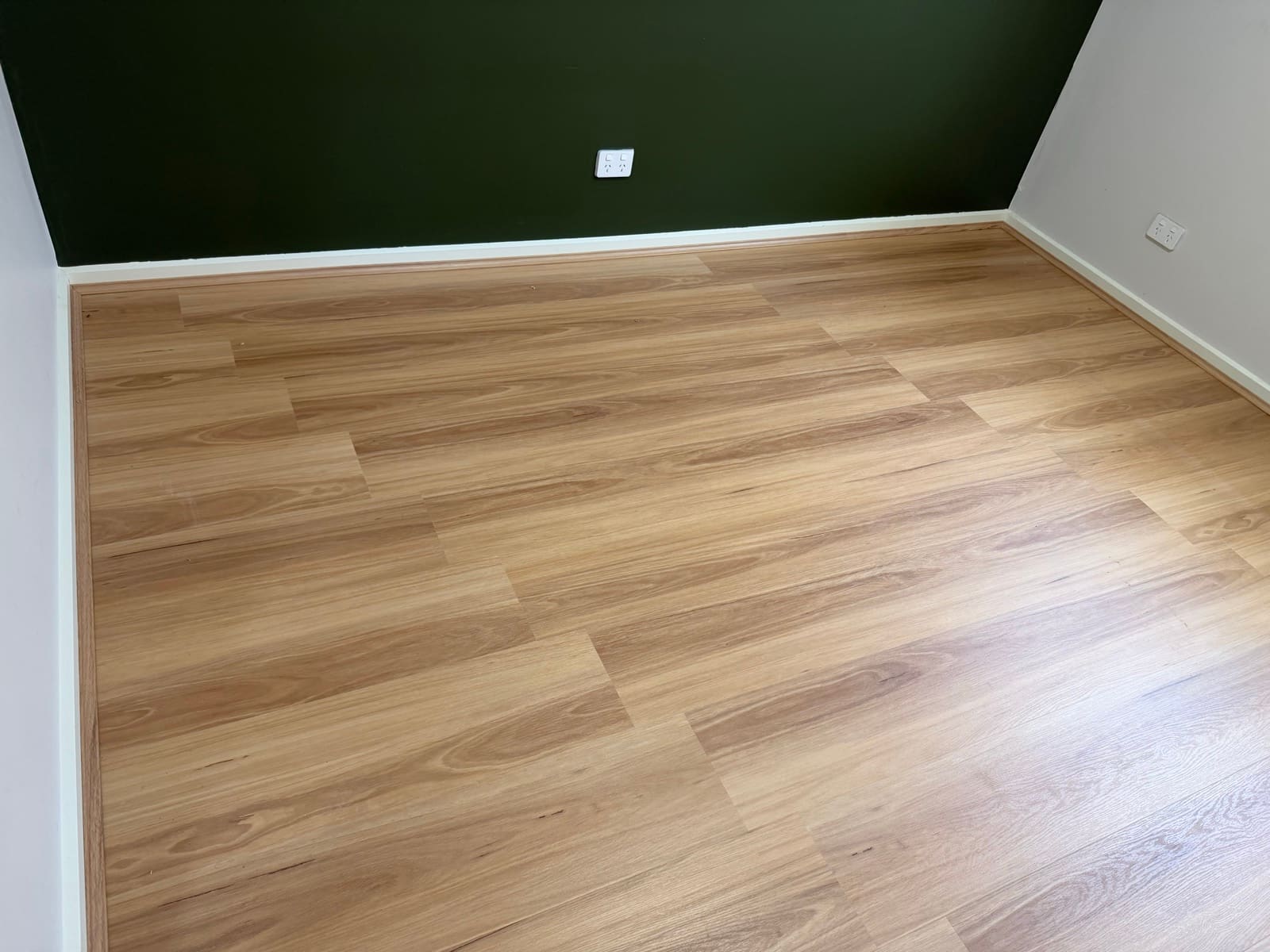 Timber-look hybrid flooring installed in a room with a dark green feature wall and white skirting