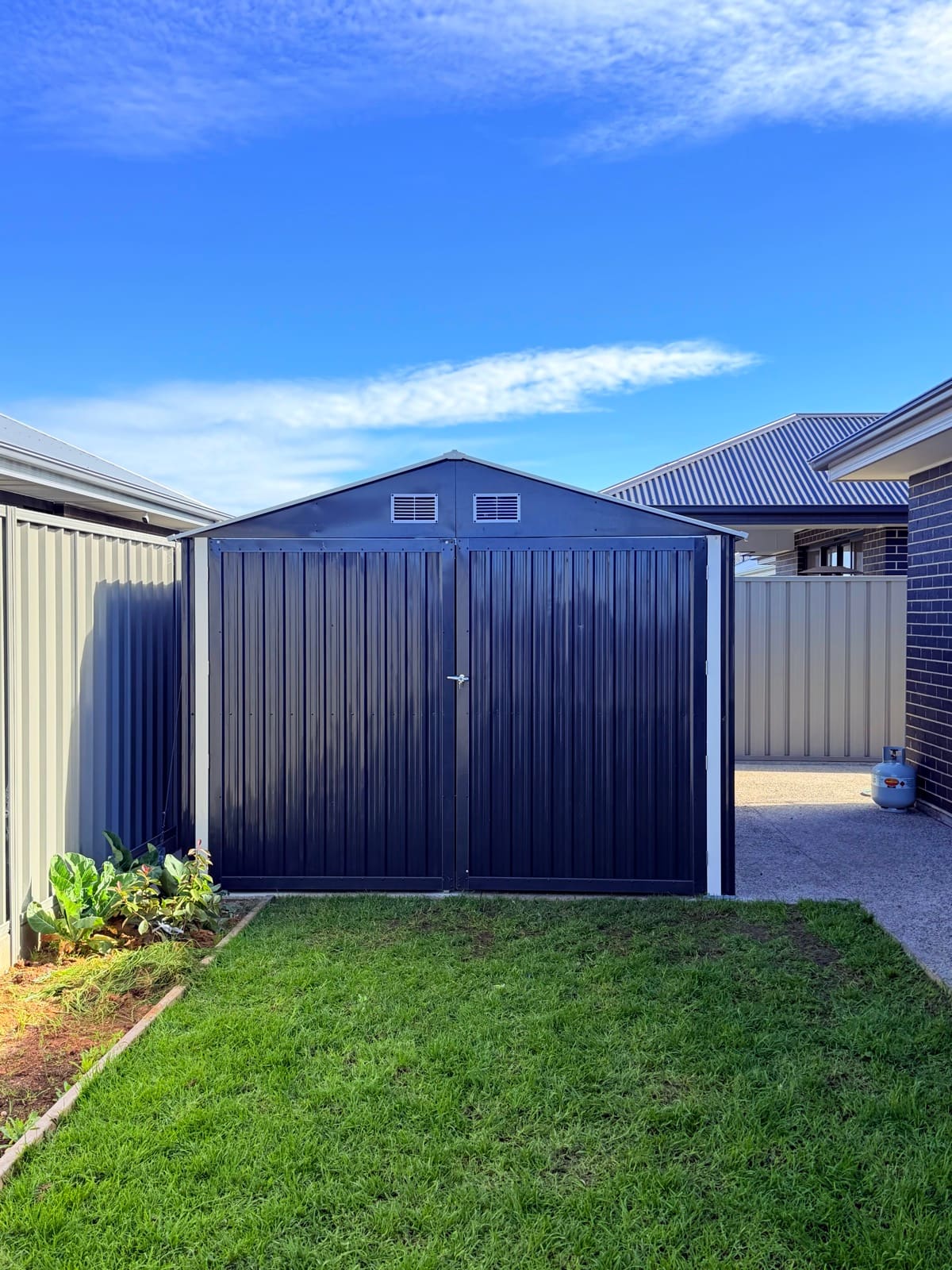 Front view of a newly installed metal garden shed facing a green lawn in Adelaide